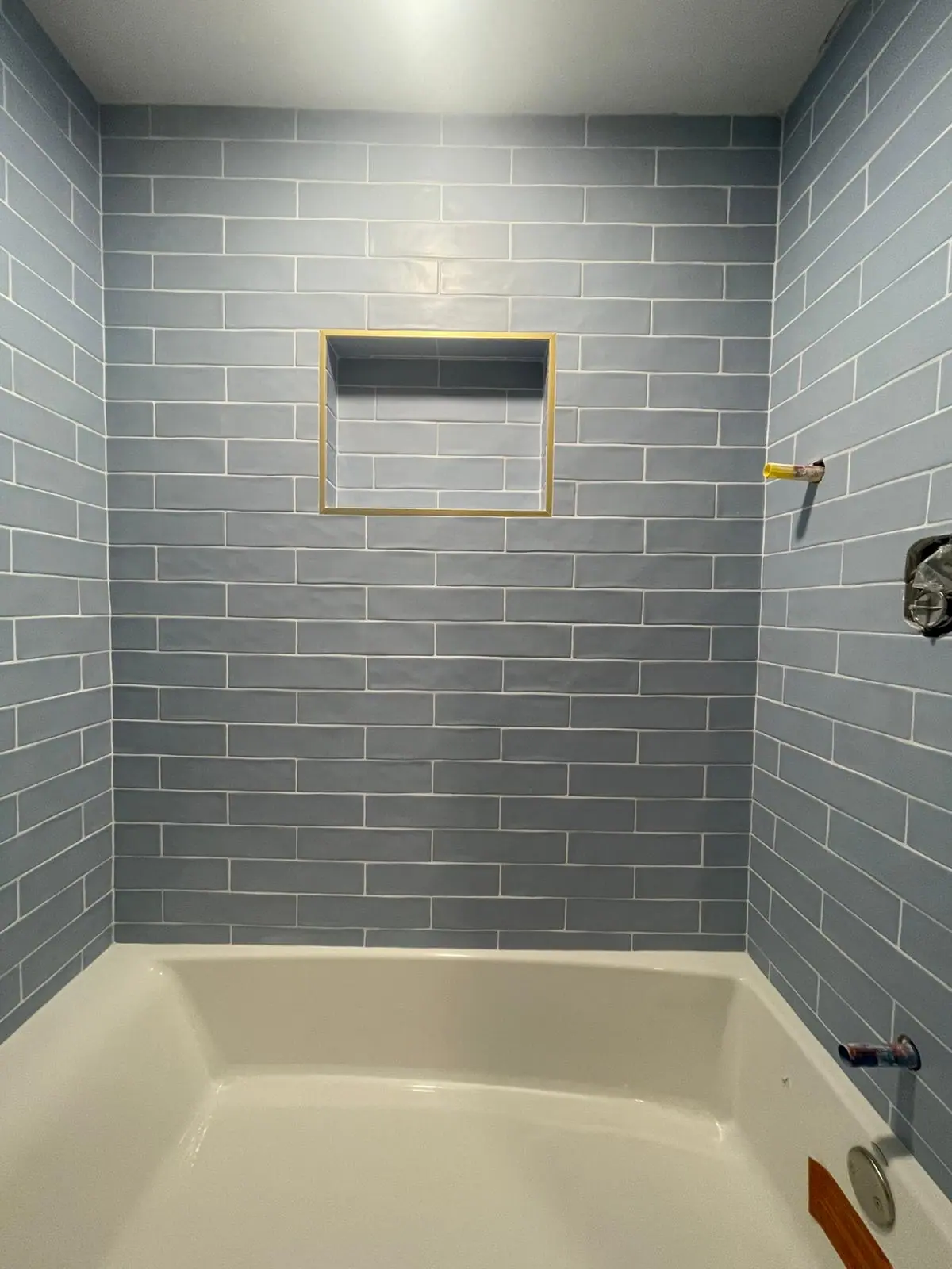 Tub surround in blue-gray subway tile with a recessed niche framed in gold trim