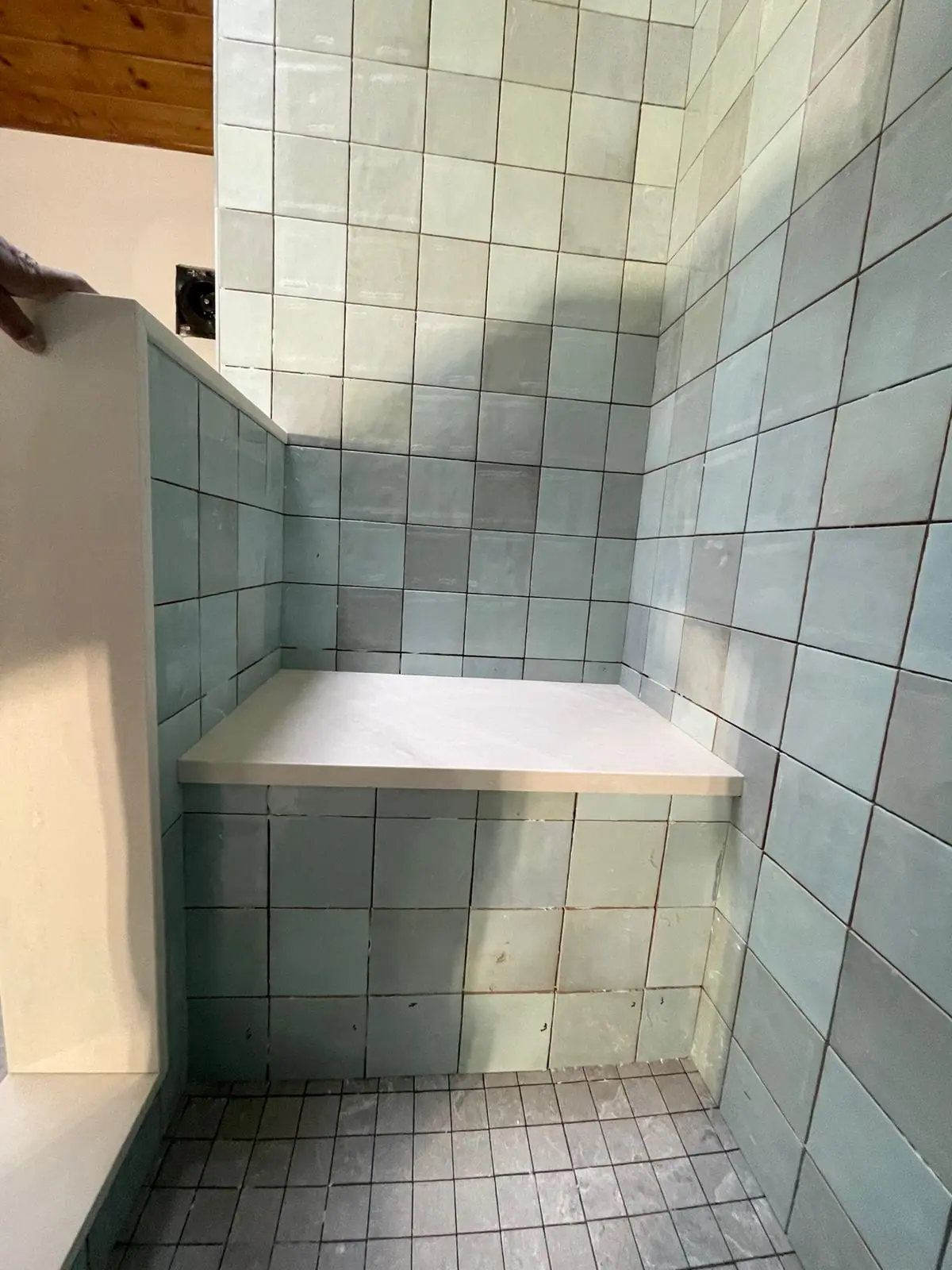 Shower bench wrapped in pale green square tile with a light stone cap