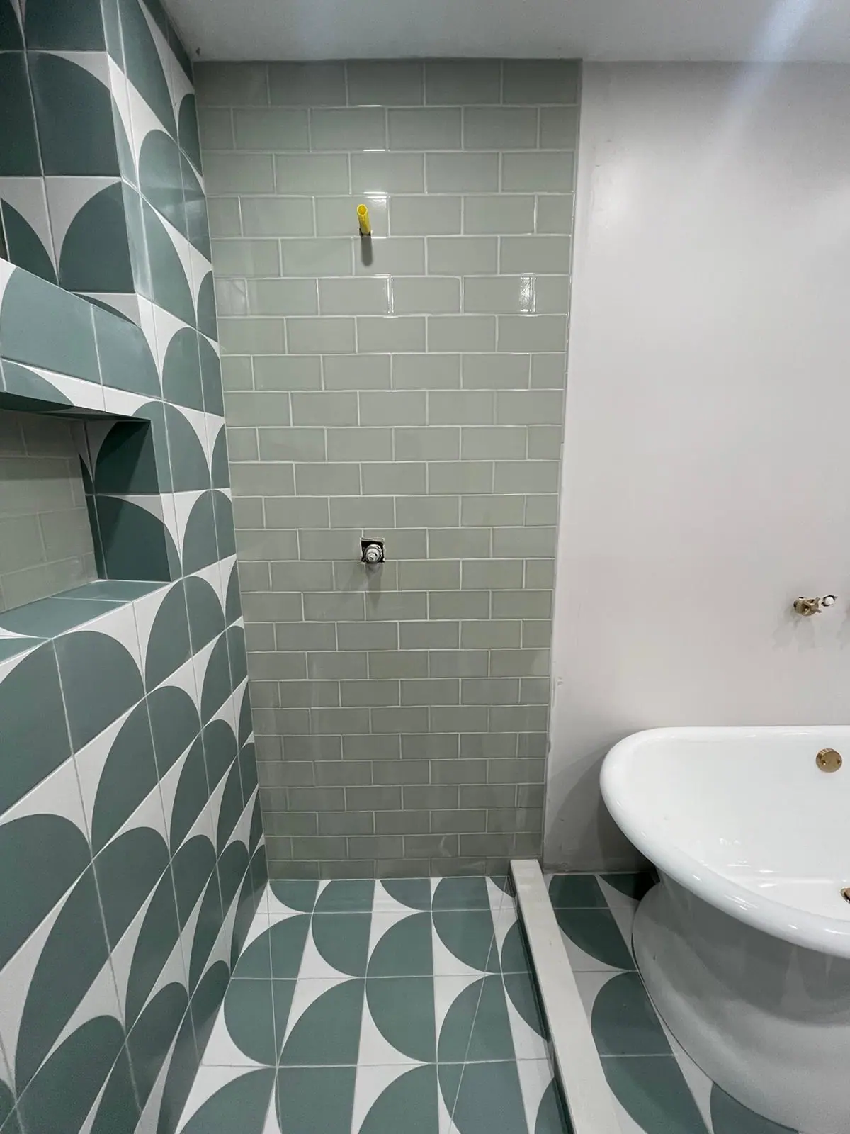 Sage glossy subway tile next to a green and white patterned tile wall that continues onto the floor
