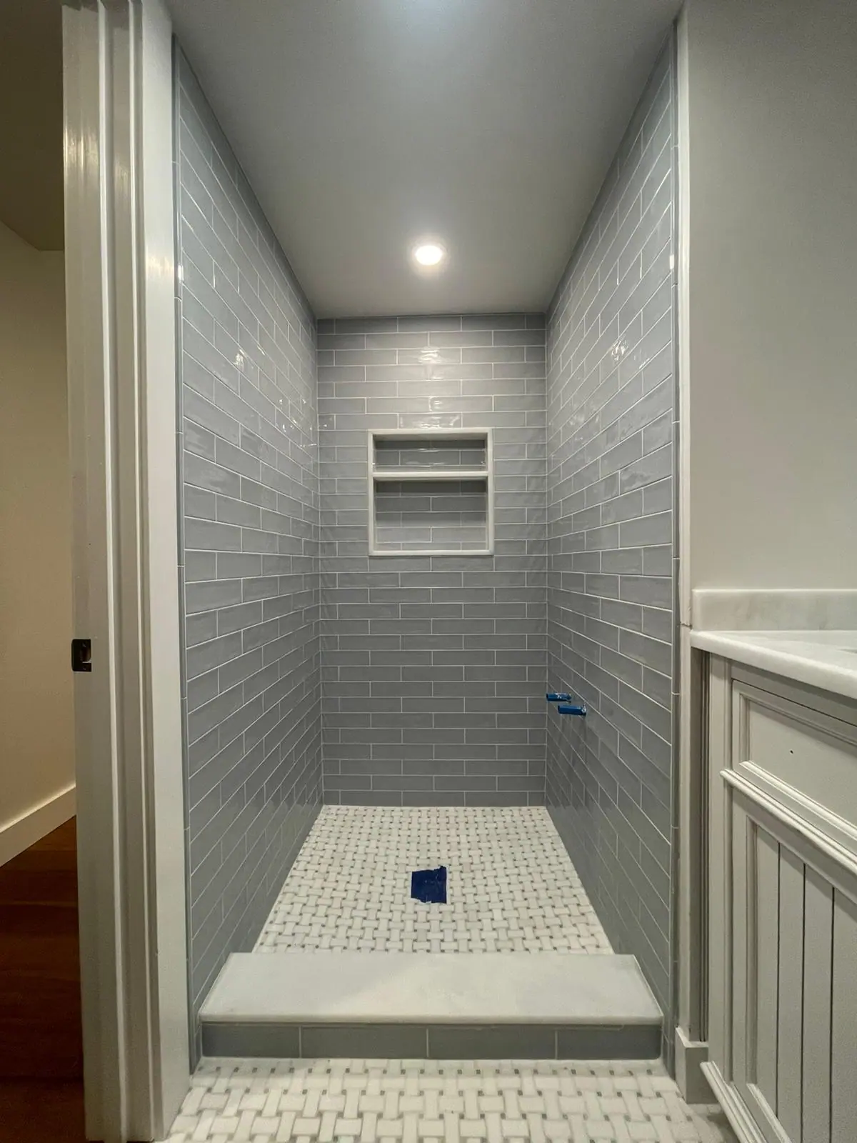 Walk-in shower with light gray subway tile, a recessed niche, a bench and a basketweave mosaic floor