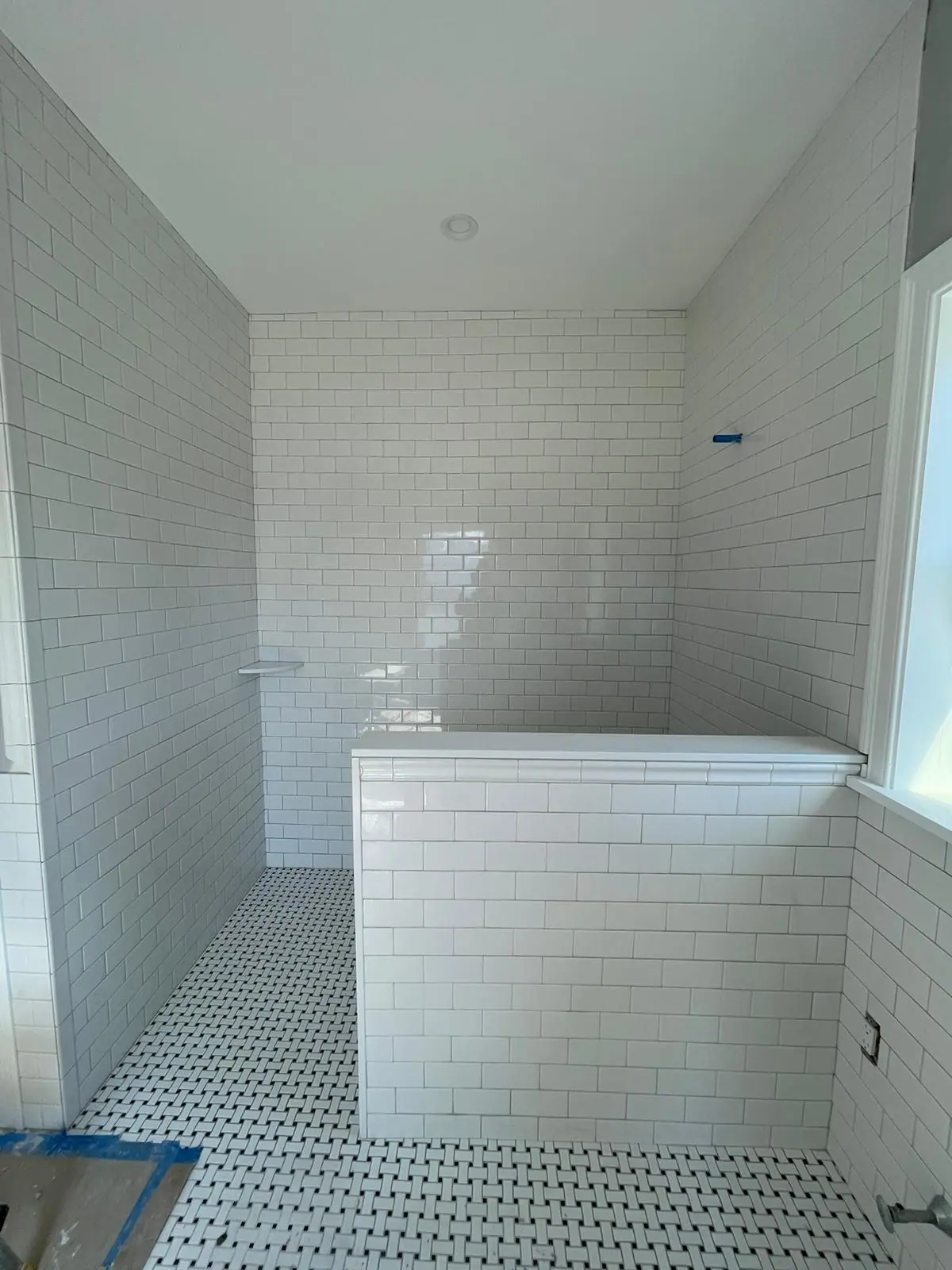 White subway tile shower with a tiled knee wall and a black and white basketweave floor